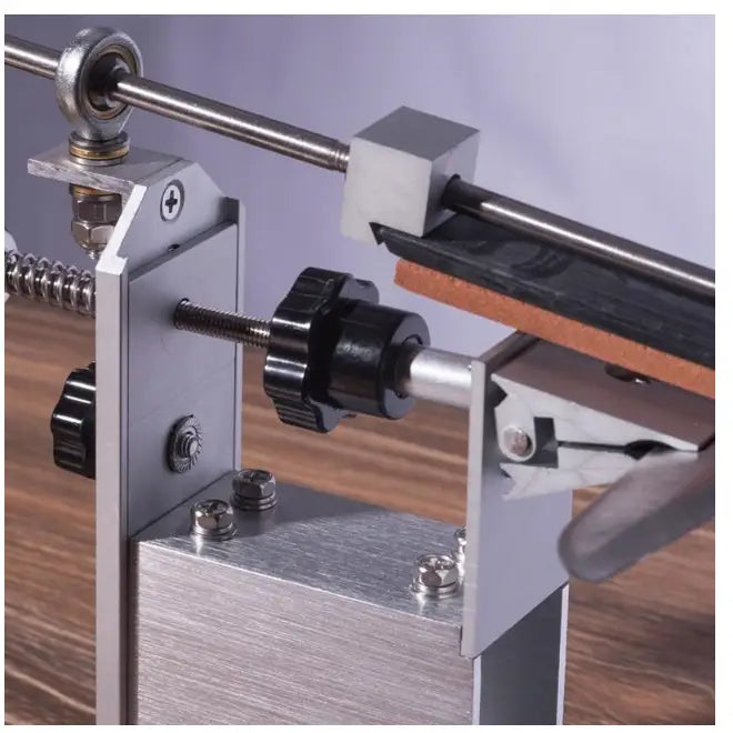 Profesjonell knivsliper, nærbilde av justerbar metalldel med sorte knotter og lærrem på trefarget underlag.