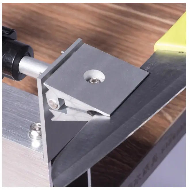 Profesjonell knivsliper med tre bryner, kniv med gult håndtak slipes i metallholder på tregulv.