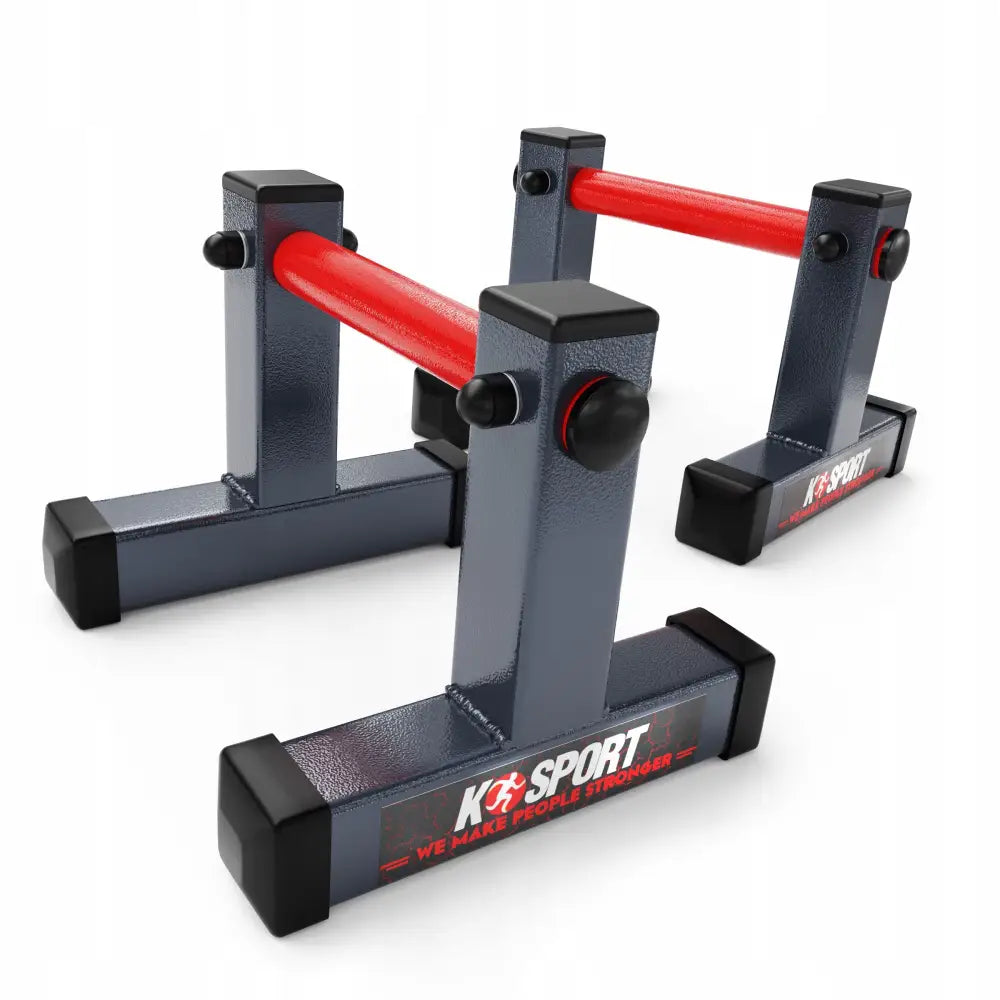 Push-up håndtak Støtter i mørk grå metall med røde tverrstenger, sett fra skrå vinkel mot hvit bakgrunn.