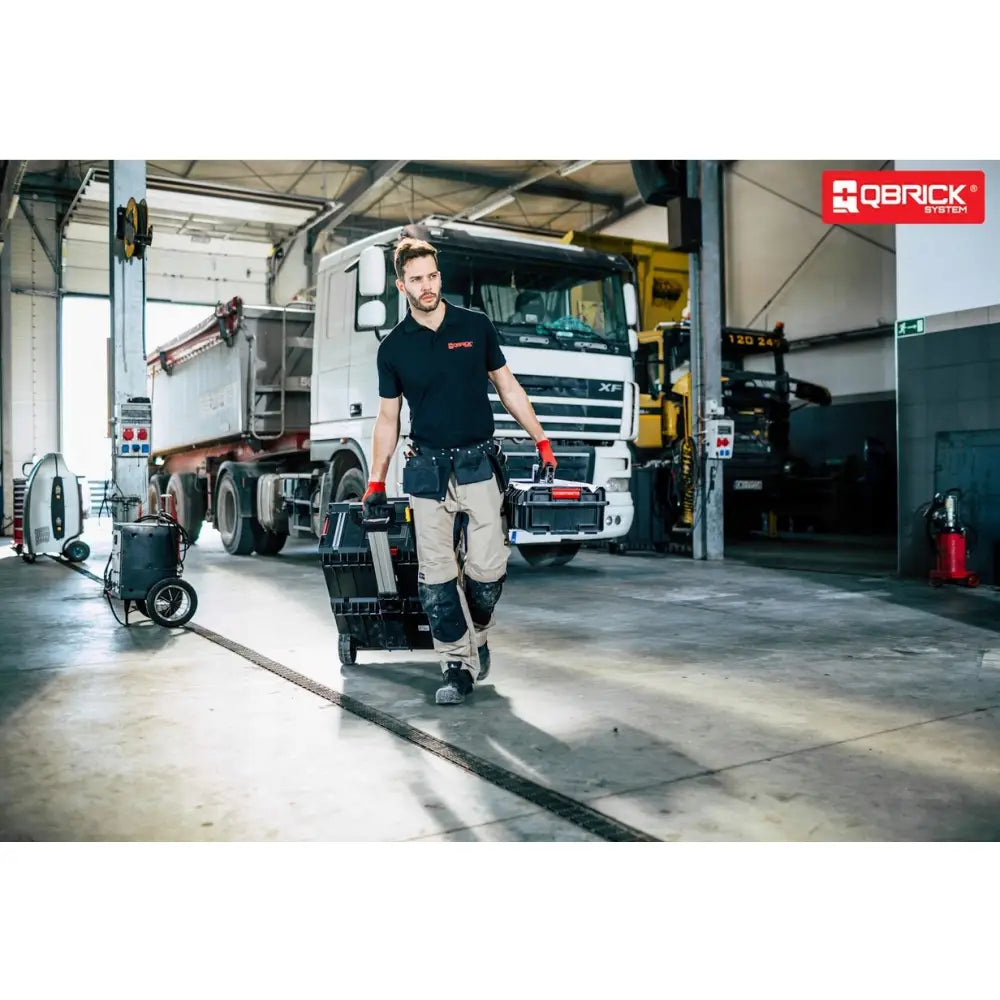 Qbrick System One Cart Techniker Set, bæres av mann i arbeidsklær foran lastebil i lyst industrilokale.