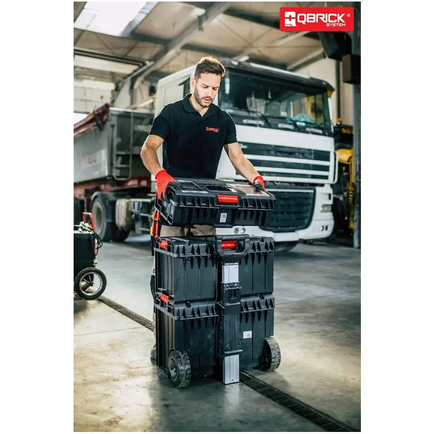 Qbrick System One Cart Techniker Set, trilles på hjul av en mann i verksted med lastebil i bakgrunnen.