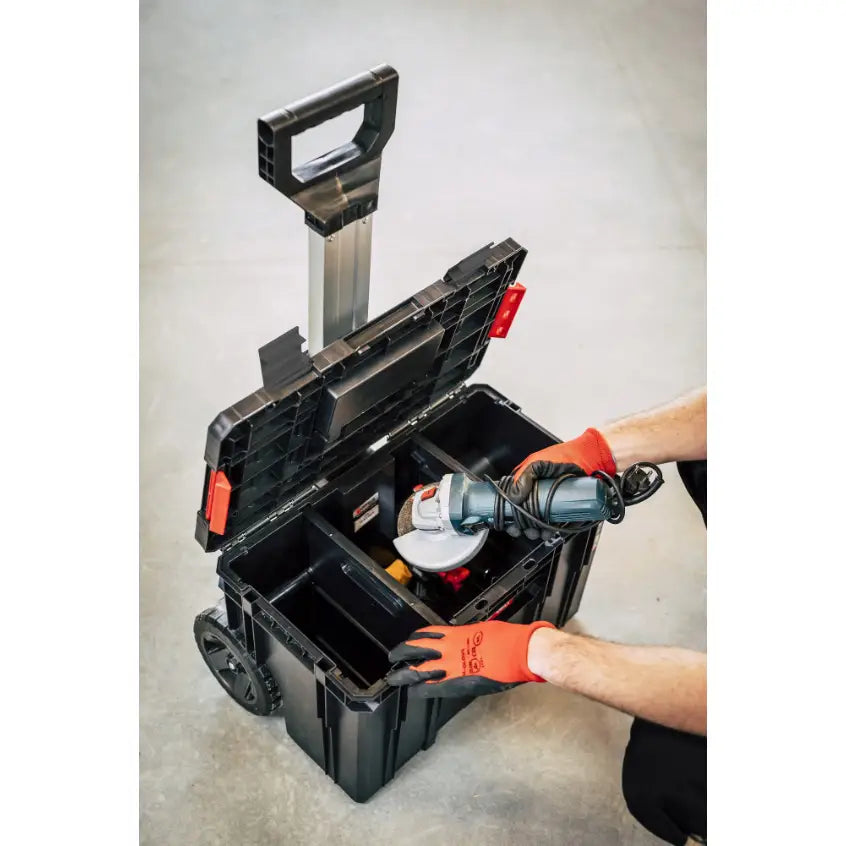 Qbrick verktøykasse med åpent lokk, vinkelsliper plasseres i kassen av person med røde hansker.