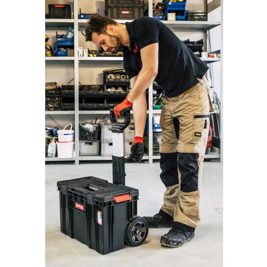 Qbrick verktøykasse sett, sidevisning med hjul og teleskophåndtak brukt av person i verksted.