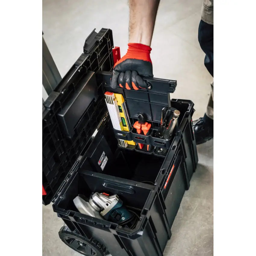 Qbrick verktøykasse sett, åpen ovenfra med verktøy og vater i uttakbar innsats løftet av hanskekledd hånd.