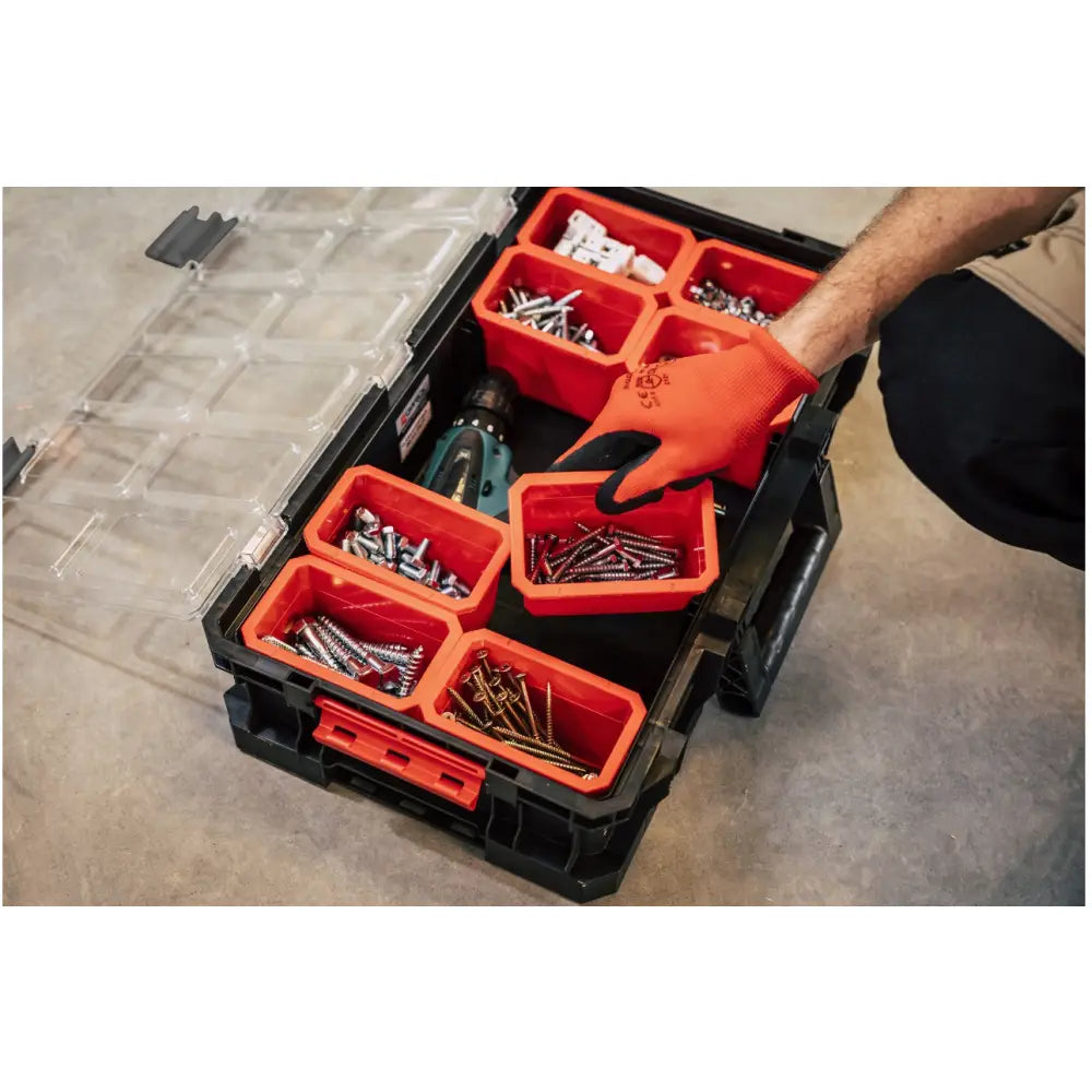 Qbrick verktøykasse, sortimentsboks i svart plast med oransje rom og hånd med hanske som løfter et rom.