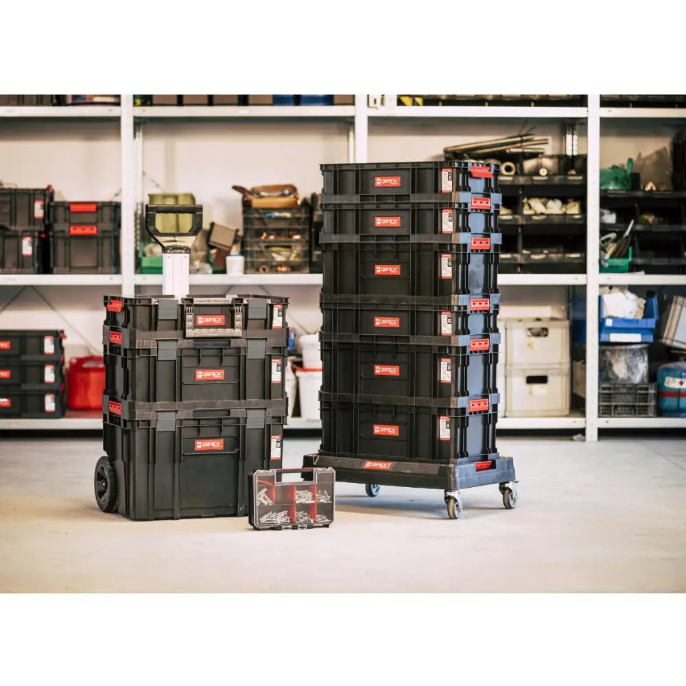 Qbrick verktøykasse sett stablet på hjul, med røde detaljer, plassert foran verkstedhyller.
