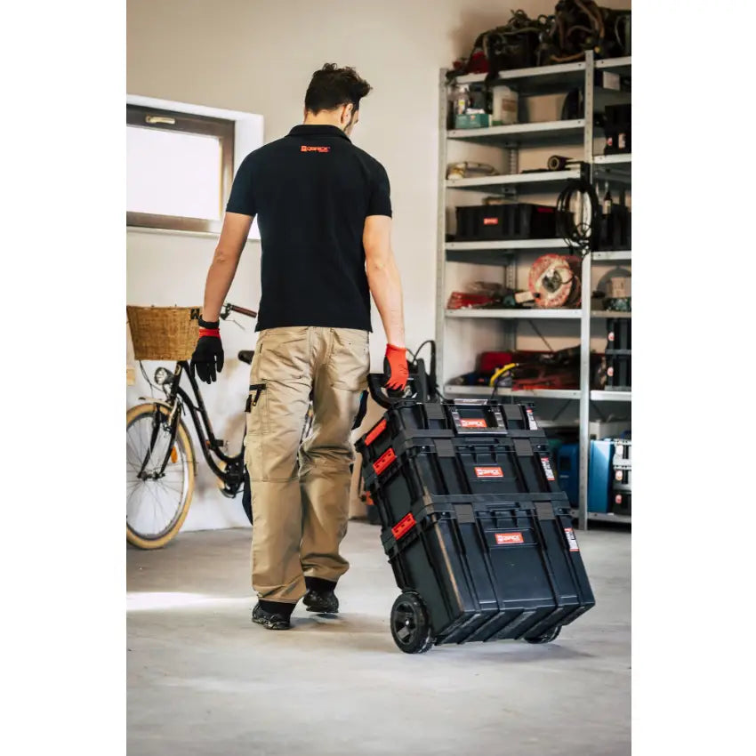 Qbrick verktøykasse sett Two 6I1, trilles på hjul av person i verksted med hyller og sykkel bak.