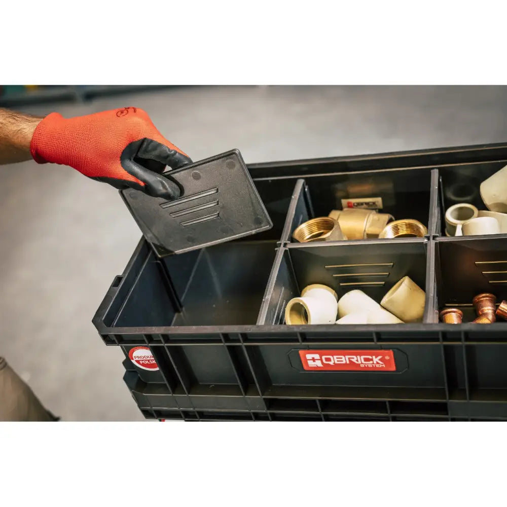 Qbrick verktøykasse sett, åpen sort boks med rørdeler, rød hanske løfter skillevegg over rommene.