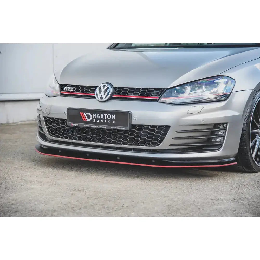 Front lip på VW Golf 7 GTI med svart og rød spoiler, GTI-emblem og bikubemønstret grill.