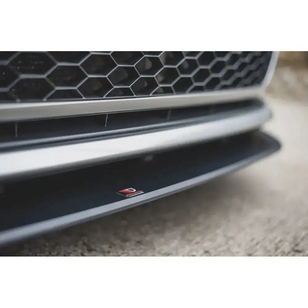 Frontspoiler VW Golf 7 GTI i sort plast, nærbilde med bikubemønstret grill og rød-hvit logo foran.