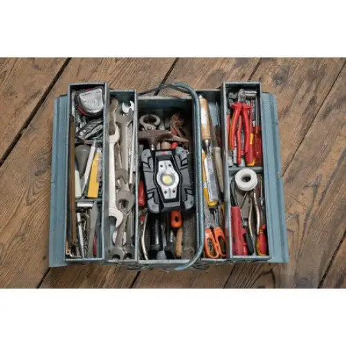 Åpen metall verktøykasse sett ovenfra med skiftenøkler, skrutrekkere, tang og målebånd på tregulv.