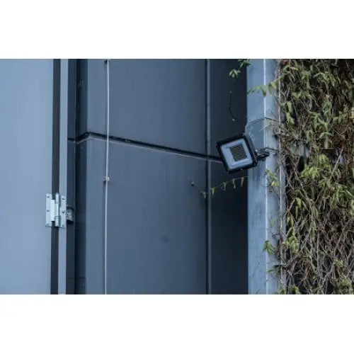 LED reflektor JARO 14060 montert på grå vegg, sideprofil med synlig moderne panel og grønn vegetasjon.