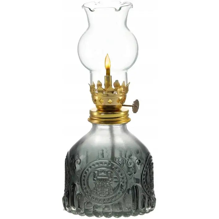 Retro oljelampe med mørk dekorert glassfot, messingbrenner og buet glass-skjerm, tent flamme synlig.