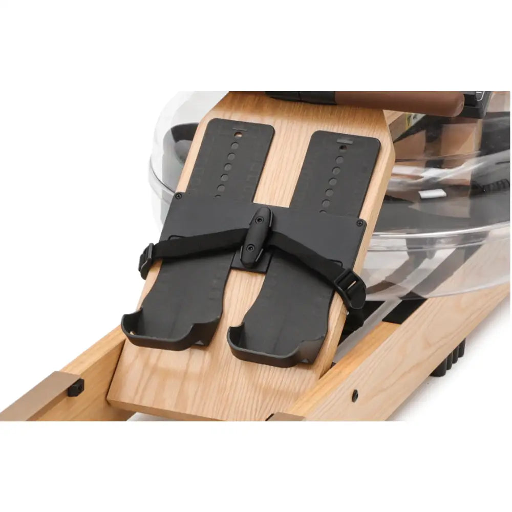 Romaskin med to svarte fotstøtter og justerbare stropper på lyst treverk, nærbilde sett ovenfra.