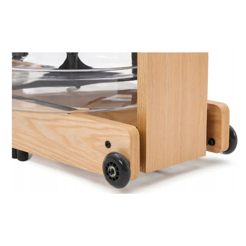 Romaskin i lyst treverk, detalj av hjørne med hjul og delvis synlig gjennomsiktig beholder.