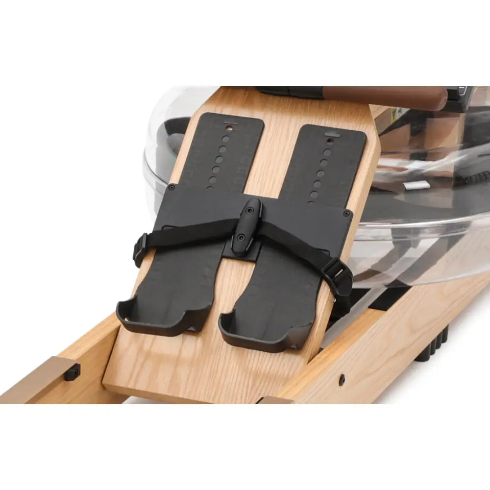 Romaskin med svarte fotplater og justerbare stropper på lyst treverk, nærbilde fra skrå vinkel.