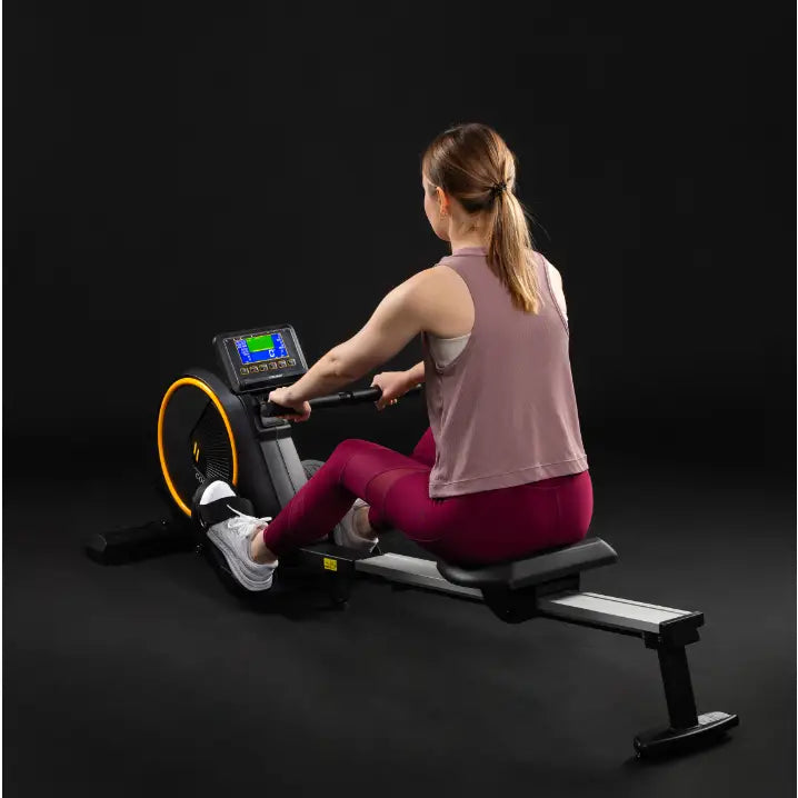 Romaskin Omega, bakfra med kvinne i trening, viser digital skjerm og gult hjul mot svart bakgrunn.