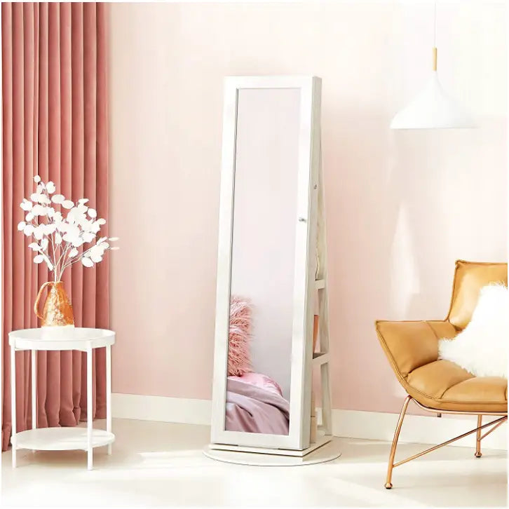 Roterende smykkeskap med speil, frontvisning i hvit ramme på sokkel i lyst rom med rosa gardiner.