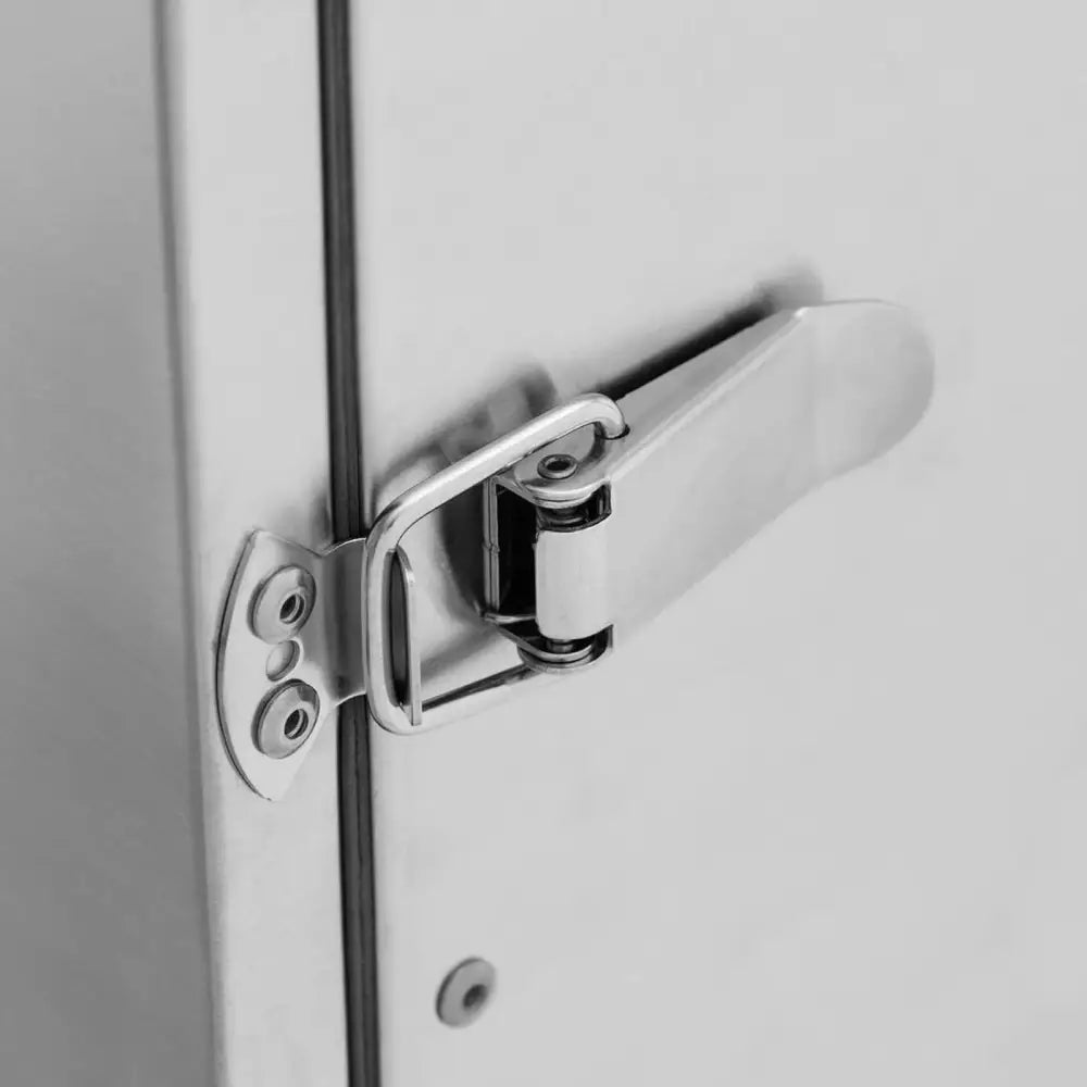 Røykovn, nærbilde av forkrommet metallspenne på lys grå overflate, fokus på selve lukkemekanismen.