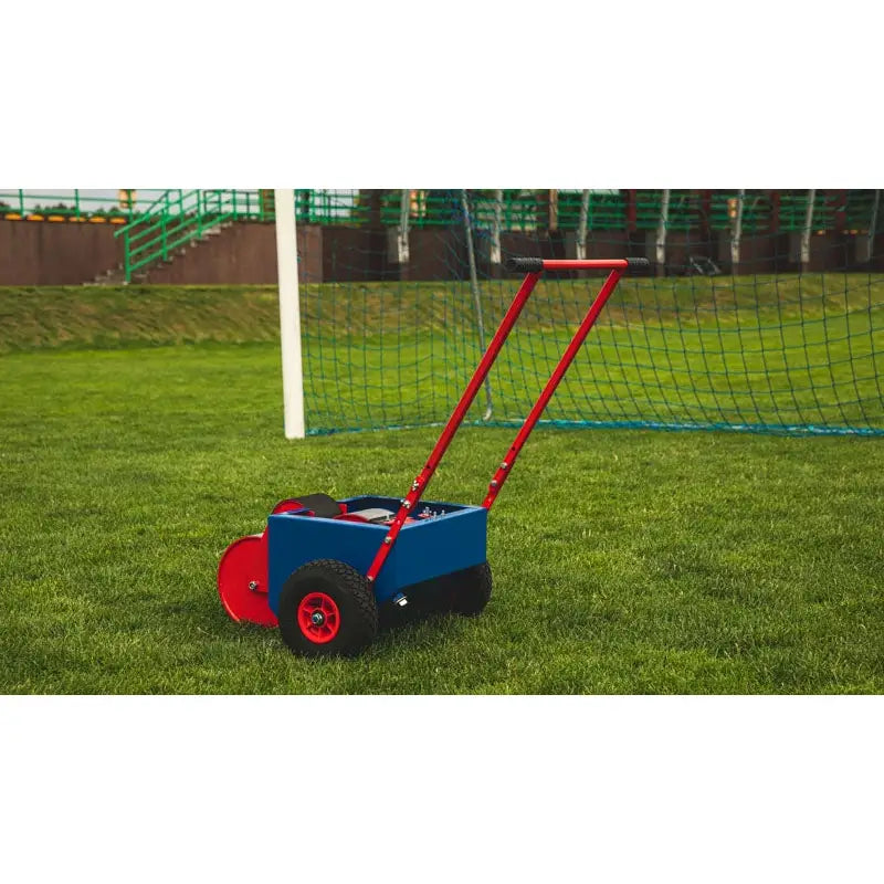 Rulleskate for linjemaling, sidevisning på gressbane med blå boks, røde hjul og håndtak foran fotballmål.