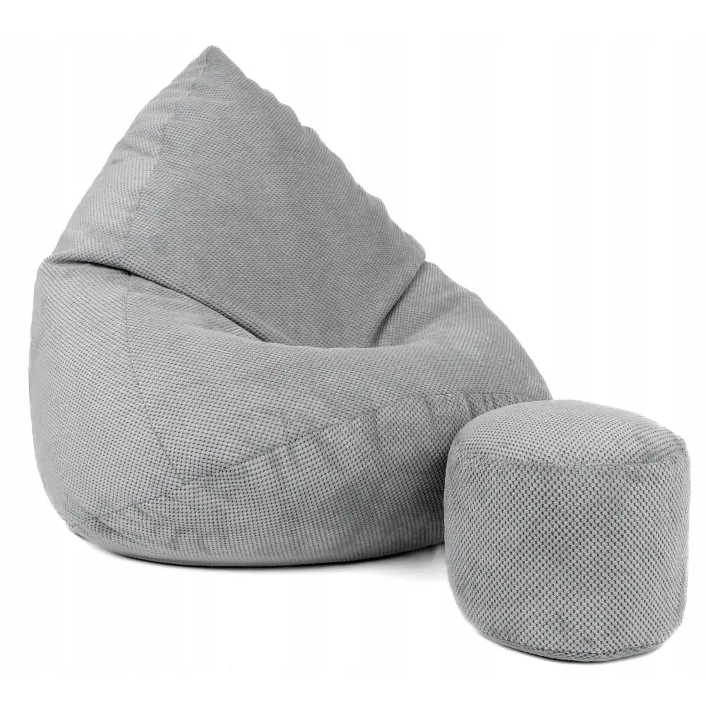 Saccosekk i plysj, lysegrå med grov tekstur og matchende puff, sett fra skrå vinkel mot hvit bakgrunn.