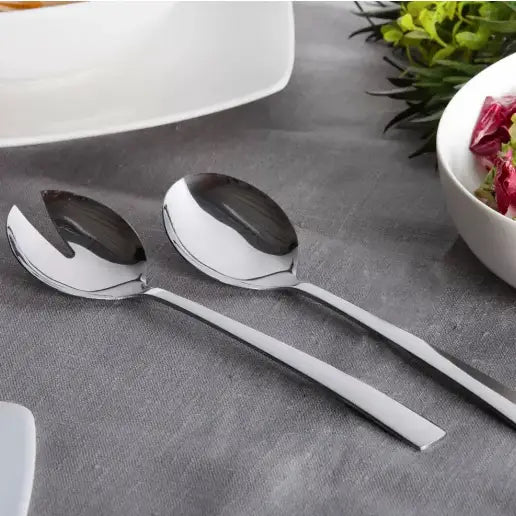 Salatskjeer i sølvfarget metall, sett ovenfra på grå duk, ett med slisset blad for servering.