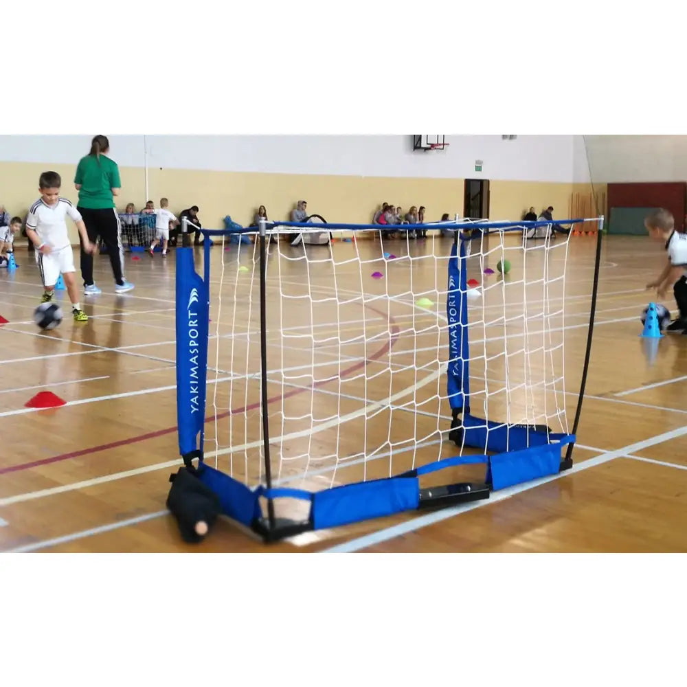 Sammenleggbar port UNI, blått fotballmål med hvitt nett brukt av barn i gymsal under fotballspill.