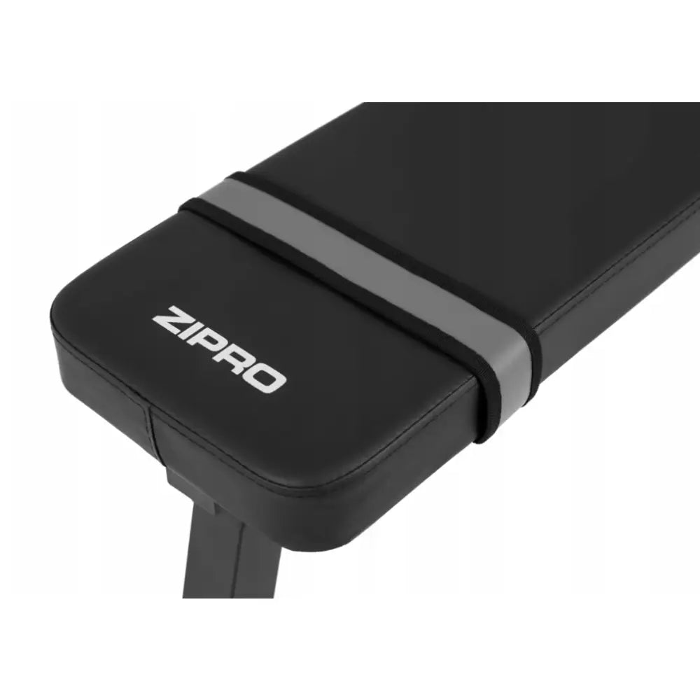 Sammenleggbar treningsbenk fra Zipro, nærbilde av svart polstring, grå stropp og tydelig logo på overflaten.