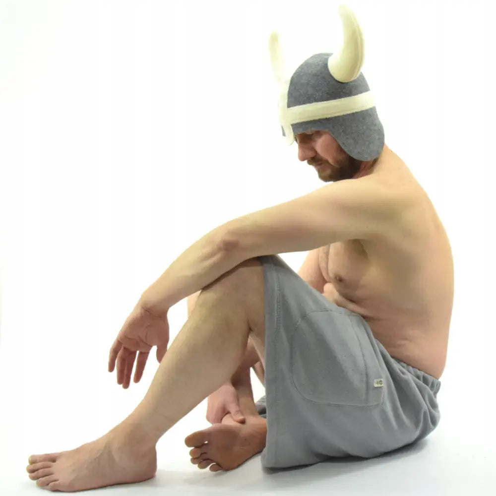 Saunasett Viking L, mann med vikinghjelm og grått frottéhåndkle sitter i profil mot hvit bakgrunn.
