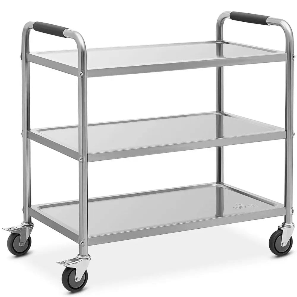 Serveringsvogn i rustfritt stål med tre hyller, sorte håndtak og hjul med bremser, sett fra siden.