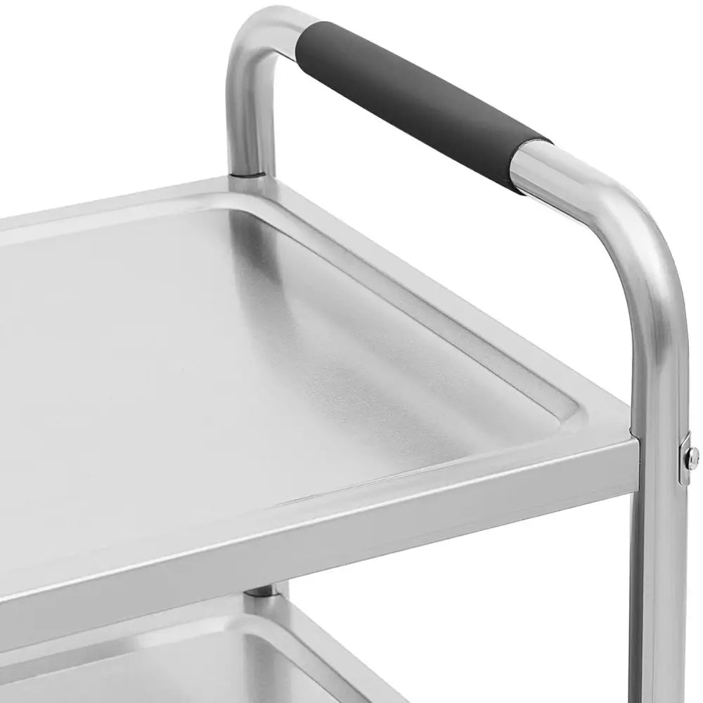 Serveringsvogn i rustfritt stål, nærbilde av sklisikkert sort håndtak og øverste hylle sett fra siden.