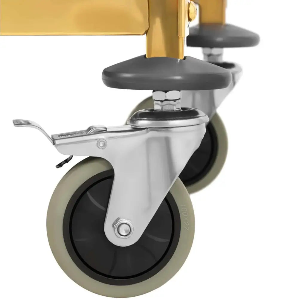 Serveringsvogn, nærbilde av grå og svarte hjul med sølvdetaljer og brems under gult metallstativ.
