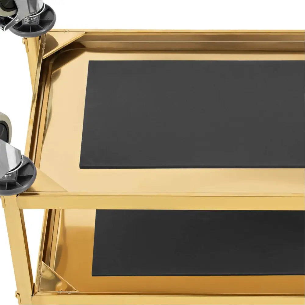 Serveringsvogn med gullramme, nærbilde av to sorte hyller sett ovenfra med hjul synlige i hjørnet.