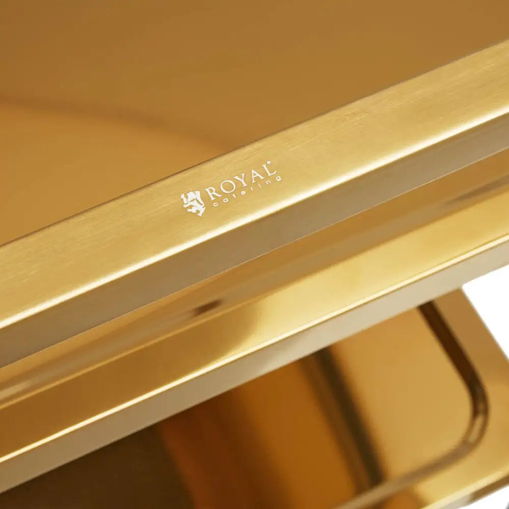 Serveringsvogn i gull, nærbilde av metallhjørne med gravert Royal Catering-logo og blank overflate.