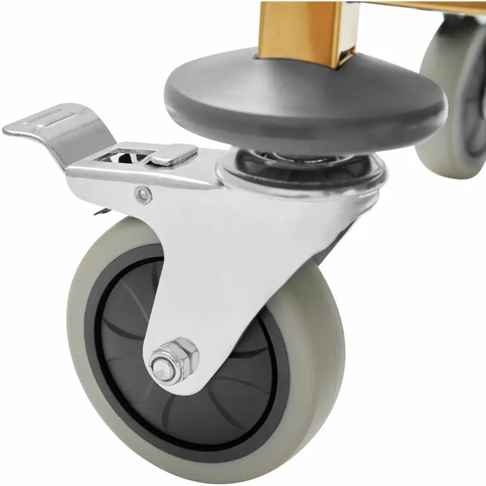 Grått plastikkhjul med sort felg og brems, montert på gullfarget metallramme til serveringsvogn.