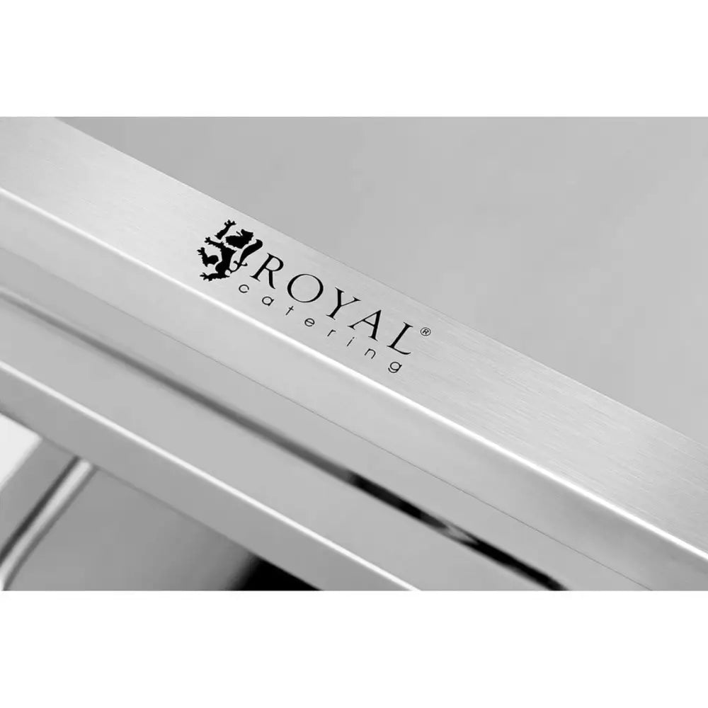 Serveringsvogn med 3 hyller, nærbilde av børstet stål med tydelig svart «Royal Catering»-logo på metallkant.