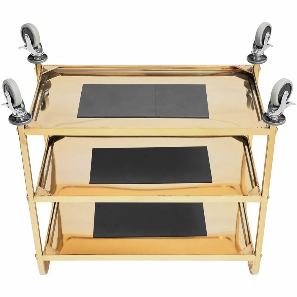 Serveringsvogn i gull, toppvinkel som viser tre hyller med svarte matter og fire hjul i hvert hjørne.