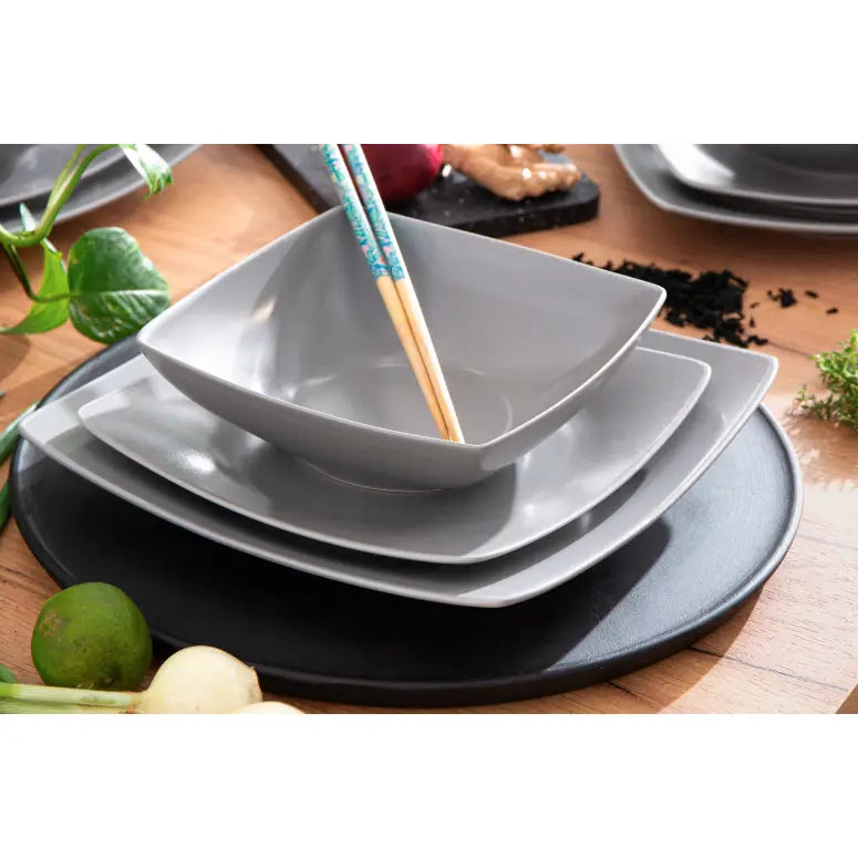 Epiri servise i matt grå keramikk, firkantede skåler og tallerkener stablet med spisepinner, grønnsaker rundt.
