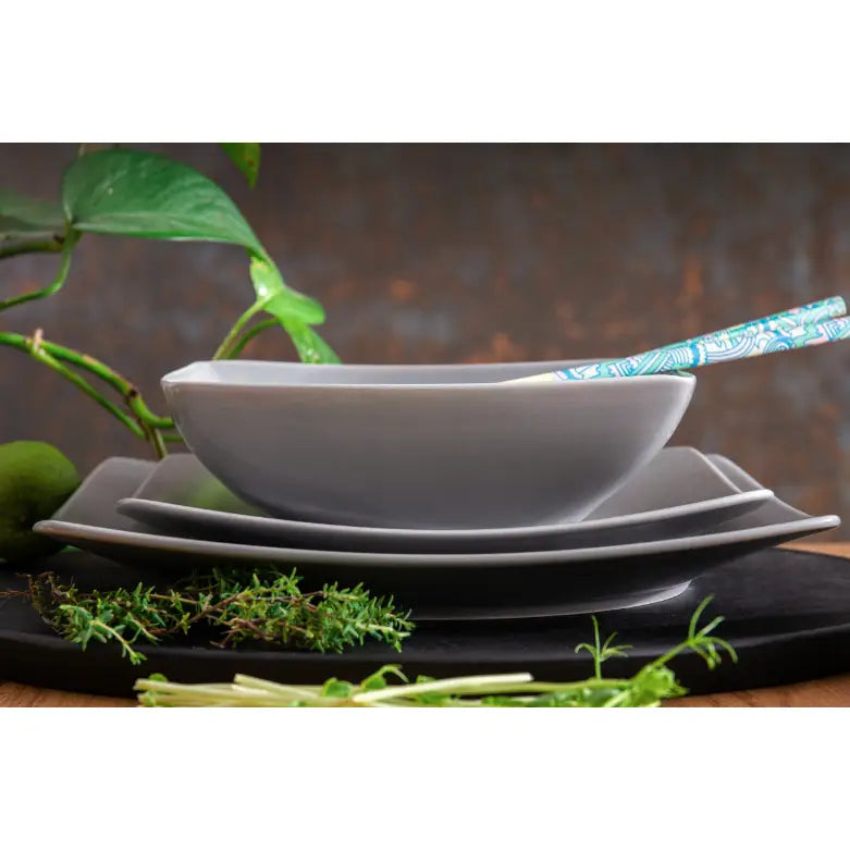 Epiri servise i matt grå keramikk, stablet bolle og tallerkener med urter og spisepinner foran.