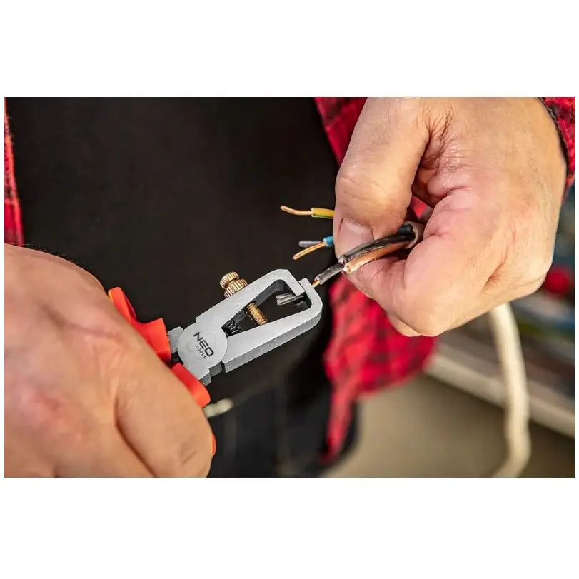 Avbitertang med oransje håndtak i bruk for avisolering av ledning, nærbilde av arbeidende hender.