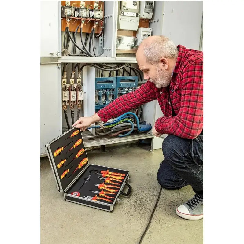 Sett med tang og skrutrekkere, mann i rød rutete skjorte jobber foran sikringsskap med åpent verktøyskrin.