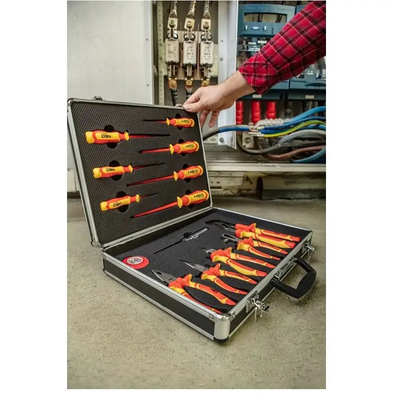 Sett med tang og skrutrekkere, åpen koffert på gulv med gule og røde verktøy, hånd tar ut ett verktøy.