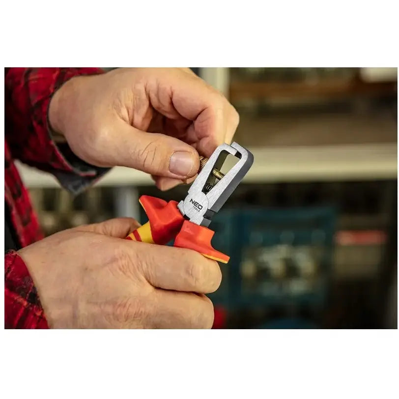 Avbitertang med rød og gul isolert håndtak, nærbilde mens den kutter en elektrisk ledning.