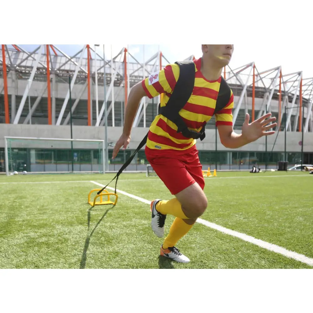 Sikkert treningsvekt 9 kg i bruk, festet med sele mens utøver løper på kunstgress med gul motstandstrener bak.
