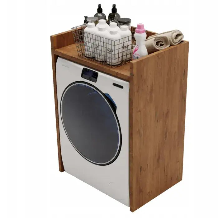 Skap for vaskemaskin i lyst tre, skråvisning med synlige vaskemidler, trådkurv og sammenrullede håndklær.