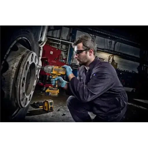 Slagtrekker Dewalt DCF899P2 i bruk på stort hjul, fokus på verktøyets design og verkstedmiljø.