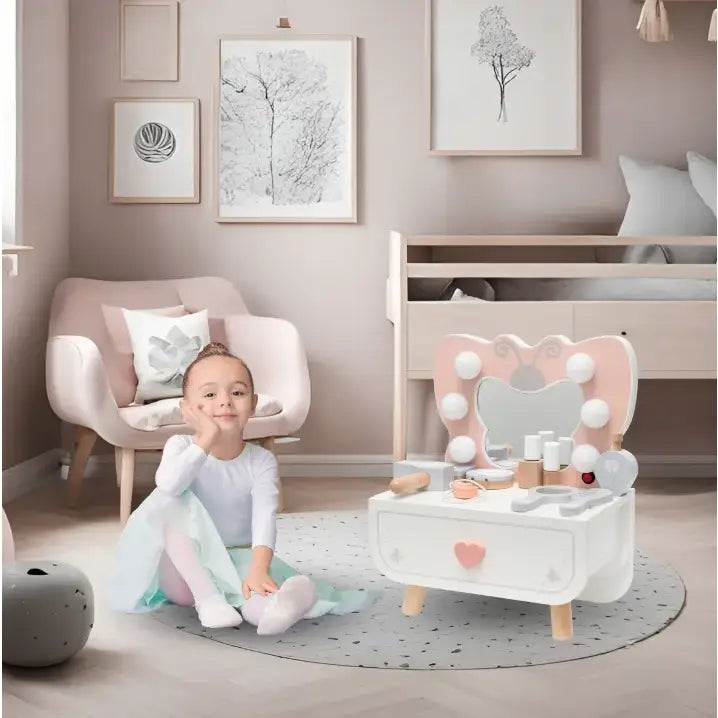 Sminkebord for barn i hvitt og rosa tre, med speil og pynt, vist på lyst barnerom sammen med barn på teppe.