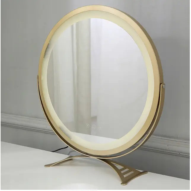 Sminkebord i loft-stil, rundt LED-speil med gullramme og metallstativ på hvit bordplate, sett fra siden.