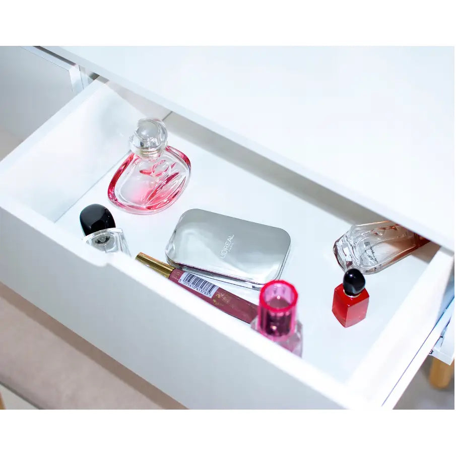 Sminkebord med LED-speil, åpen hvit skuff sett ovenfra med sminke og parfyme i rosa og sølv.