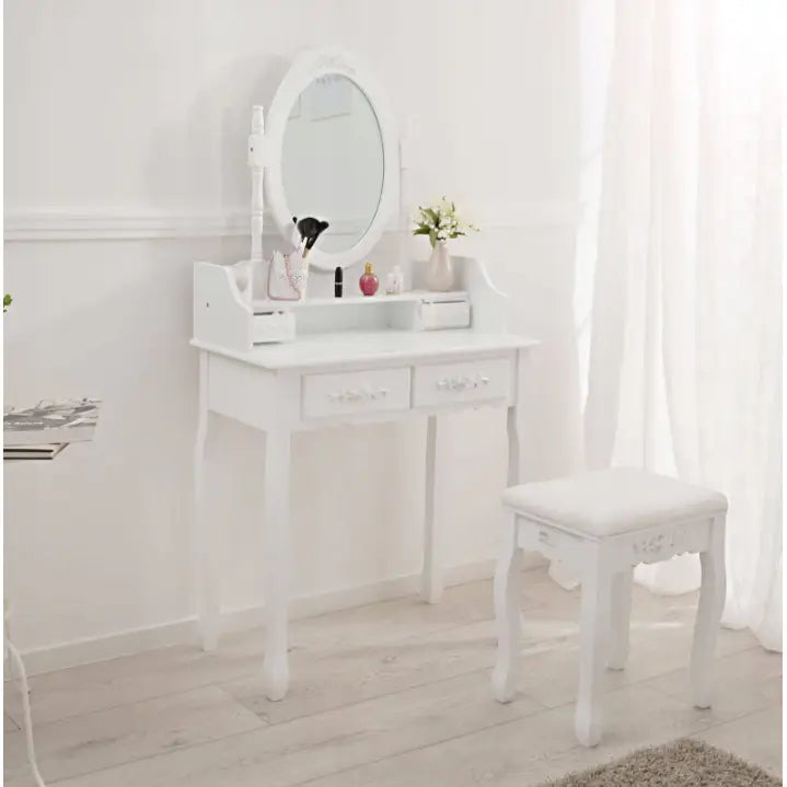 Sminkebord med speil i hvitt, to skuffer, dekorative utskjæringer og polstret krakk, sett fra skrå vinkel.